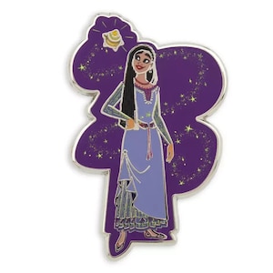 May include: A purple enamel pin featuring a cartoon woman with long dark hair wearing a blue dress and a gold necklace. She is standing in front of a purple background with gold stars and a gold lamp.