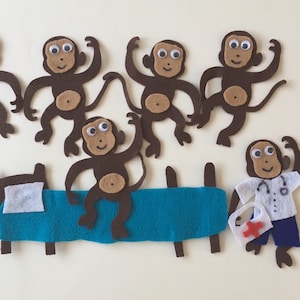 Peut inclure: Cinq marionnettes de singe en feutre marron avec des yeux globuleux, une marionnette de singe en feutre marron habillée en médecin avec un stéthoscope et une trousse de premiers soins avec une croix rouge, et une marionnette de singe en feutre marron habillée d'une chemise rose avec un cœur rouge et une jupe violette.
