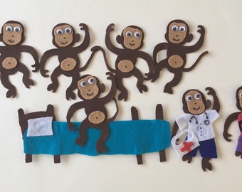May include: Five brown felt monkey puppets with googly eyes, one brown felt monkey puppet dressed as a doctor with a stethoscope and a red cross first aid kit, and one brown felt monkey puppet dressed in a pink shirt with a red heart and a purple skirt.