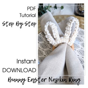 Könnte beinhalten: Ein weißer gehäkelter Hasen-Serviettenring mit Holzbasis. Der Serviettenring liegt auf einer beigefarbenen Serviette und einem gemusterten Platzdeckchen. Der Text "PDF Tutorial Step By Step Instant DOWNLOAD Bunny Easter Napkin Ring" ist auf dem Bild.