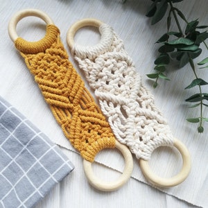 May include: Two macrame plant hangers with wooden rings. One is yellow and the other is white.