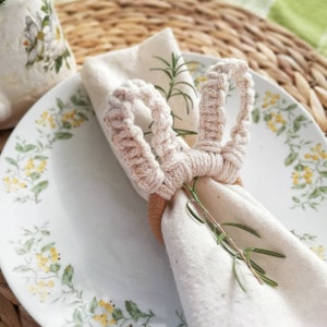 Peut inclure: Un anneau de serviette en crochet blanc en forme de lapin avec une base en bois. L'anneau tient une serviette en lin blanc avec un brin de romarin.