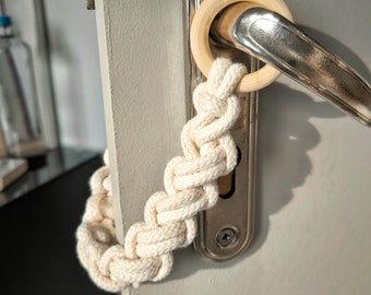 May include: A white rope door handle wrap with a wooden ring attached to a silver door handle.