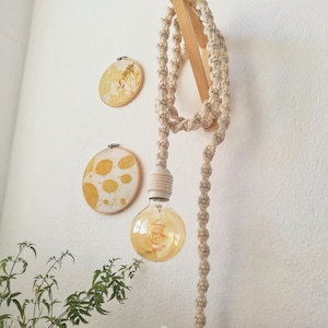 May include: A white cord light fixture with a white bulb hanging from a wooden ceiling mount. The cord is made of a thick, braided rope. The light is surrounded by three round, wooden frames with yellow pressed leaf designs.