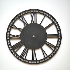 Op de afbeelding: Zwarte houten klok met Romeinse cijfers en een uitgesneden ontwerp. De wijzerplaat is leeg en klaar voor een klokmechanisme.