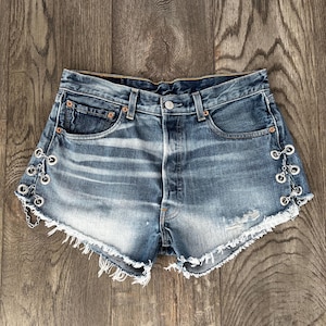 May include: A white ceramic mug with a black handle and the text "But First, Coffee" in a black, bold font. The mug is sitting on a wooden surface. The mug is approximately 4 inches tall.