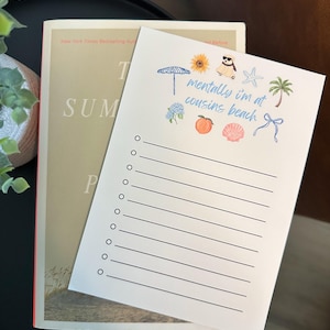 May include: A white notepad with the text "mentally i'm at cousins beach" and beach-themed illustrations, resting on a book titled "The Summer I Turned Pretty". The notepad has lines for writing and is decorated with a sunflower, peach, and seashell.