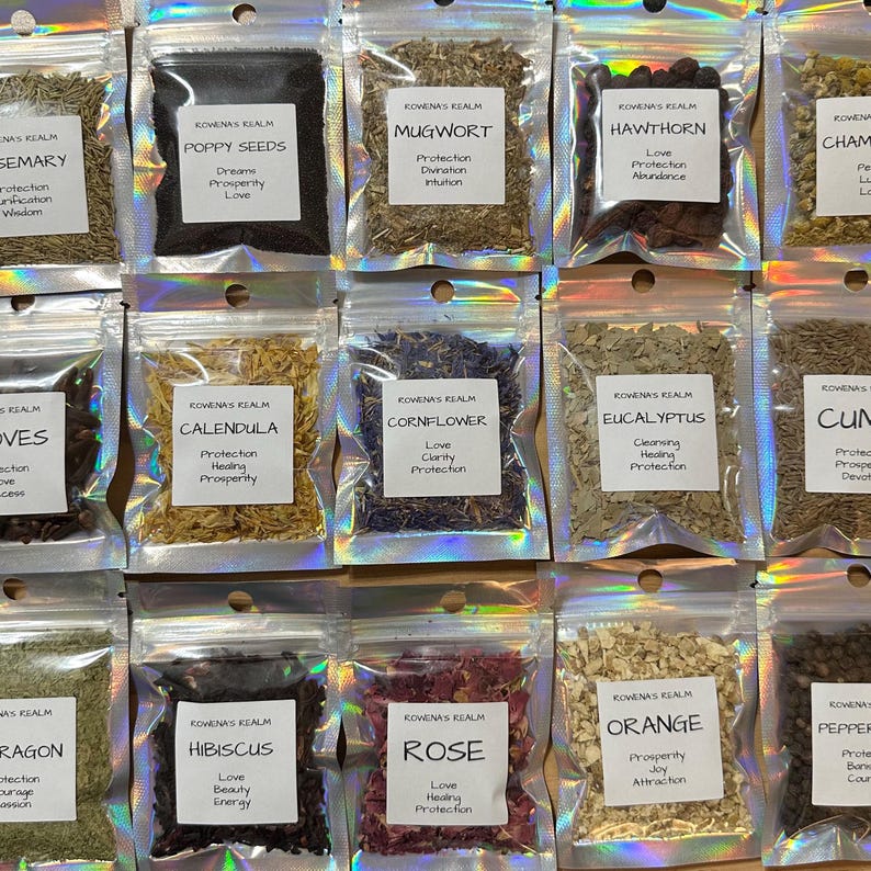 May include: A collection of small, clear, resealable bags filled with various dried herbs and seeds. Each bag has a white label with the name of the herb and associated properties, such as "Rose" for love and protection. The bags are arranged in neat rows.