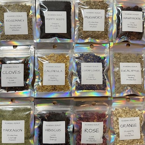 May include: Assortment of dried herbs and seeds in clear, sealed pouches. Each pouch has a white label with the herb's name and associated properties. Herbs include rosemary, poppy seeds, mugwort, hawthorn, cloves, calendula, cornflower, eucalyptus, tarragon, hibiscus, rose, and orange.