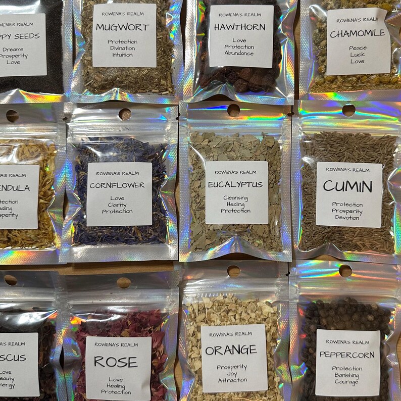 May include: A collection of small, clear, resealable bags filled with various dried herbs and spices. Each bag has a white label with the text "ROWENA'S REALM" and the name of the herb or spice, such as "Mugwort" or "Rose". The bags are arranged in rows.