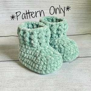May include: A pair of teal blue crocheted baby booties. The booties are made with a soft, fuzzy yarn and have a simple, classic design. The text "*Pattern Only*" is written in black at the top of the image.