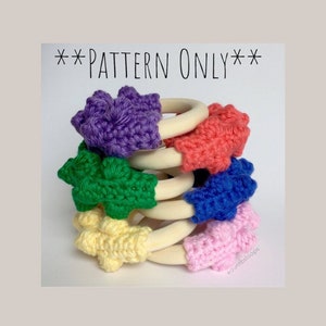 May include: A stack of six wooden teething rings with crocheted star-shaped covers in various colors, including purple, pink, red, blue, green, and yellow. The rings are stacked on top of each other, with the crocheted covers facing outwards. The text "**PATTERN ONLY**" is written in black at the top of the image.