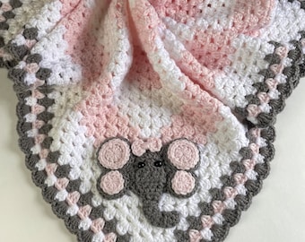 May include: A pink, white, and gray crocheted baby blanket with an elephant applique. The blanket has a scalloped edge.