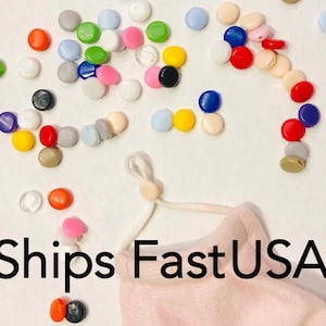 Pode incluir: Conjunto de protetores de ouvido de plástico coloridos para máscaras faciais. Os protetores de ouvido são de várias cores, incluindo vermelho, azul, verde, amarelo e branco. Os protetores de ouvido estão dispostos sobre uma superfície branca. O texto "Ships Fast USA" é visível no canto inferior direito da imagem.