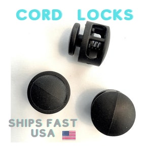 May include: Three black cord locks, also known as toggle stops, are shown on a white surface. The cord locks are used to secure cords or strings.