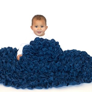 May include: A baby sitting on a large, blue, ruffled blanket. The blanket is made of soft, plush fabric and has a gathered, ruffled texture.