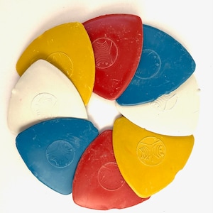 Puede incluir: Un conjunto de ocho herramientas de marcado de tela de colores dispuestas en círculo. Las herramientas tienen forma de triángulo y tienen un diseño blanco en el centro. Los colores son rojo, amarillo, azul y blanco.