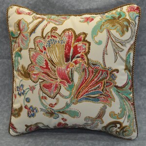 May include: A white pillow with a brown, red, and green floral pattern. The pillow has a brown trim.