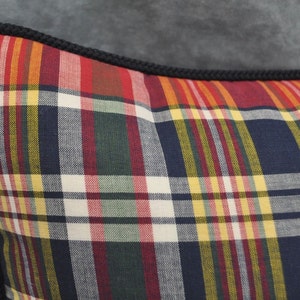 May include: A close-up of a pillow with a black and white plaid pattern. The pillow has a black cord trim around the edges.