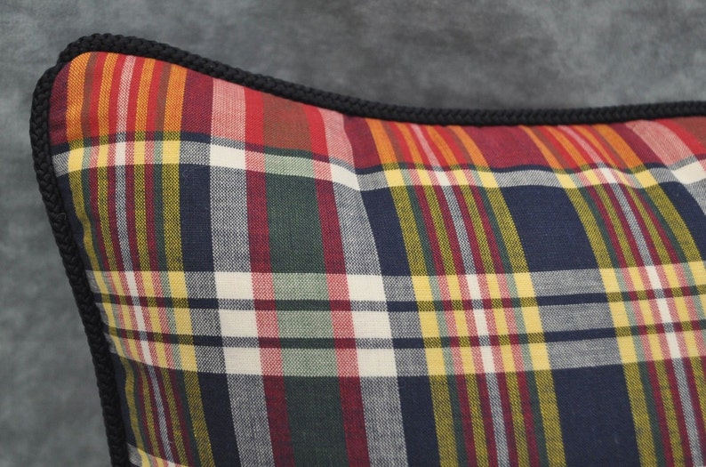 May include: A close-up of a pillow with a black and white plaid pattern. The pillow has a black cord trim around the edges.