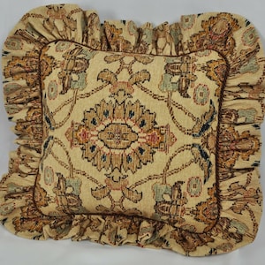 May include: A decorative cushion with a beige background and a brown, orange, and blue floral pattern. The cushion has a ruffled edge.
