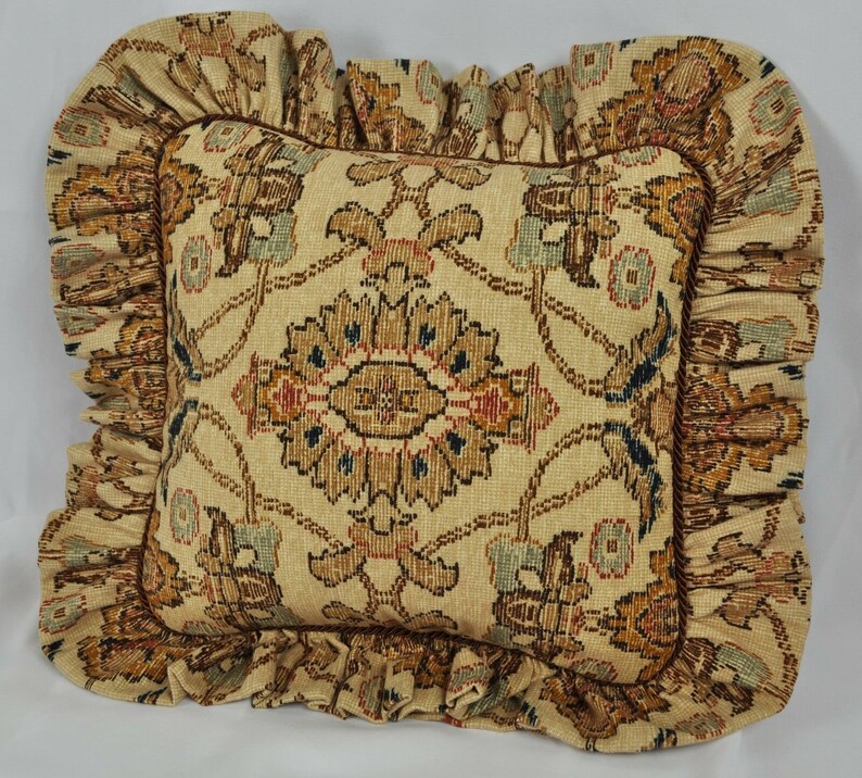 May include: A decorative cushion with a beige background and a brown, orange, and blue floral pattern. The cushion has a ruffled edge.