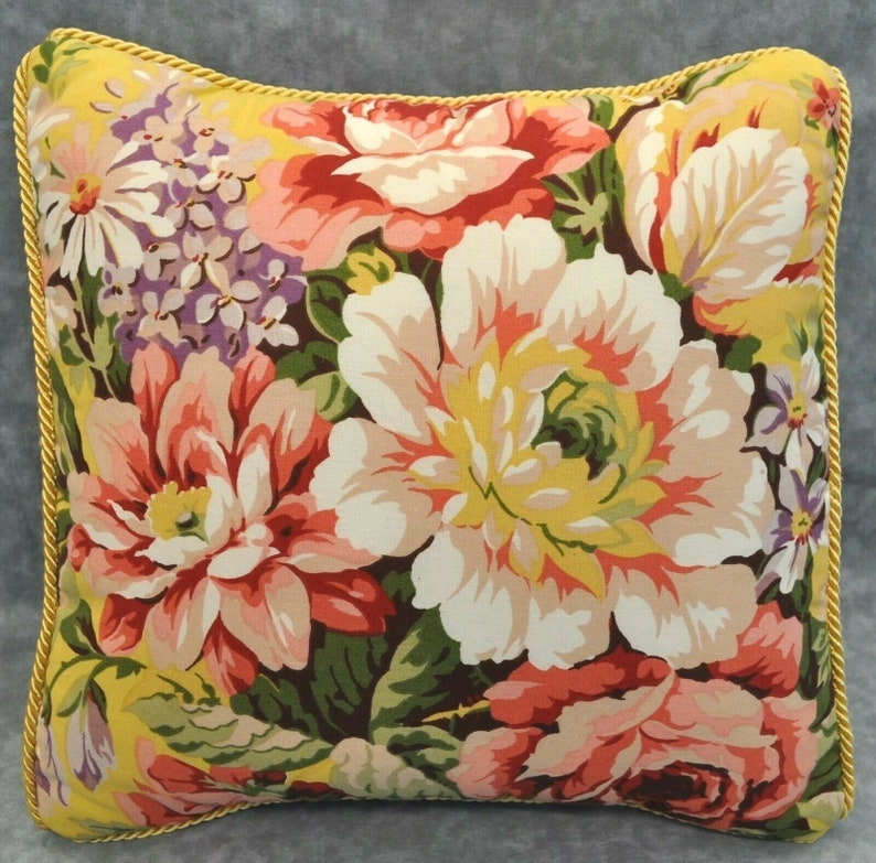 May include: A floral pillow with a yellow background and a variety of pink, red, white, and purple flowers. The pillow has a gold trim around the edges.