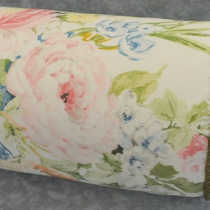 May include: A white bolster pillow with a floral print featuring pink, blue, and green watercolor flowers. The pillow has a gold trim and a white ribbon tie.