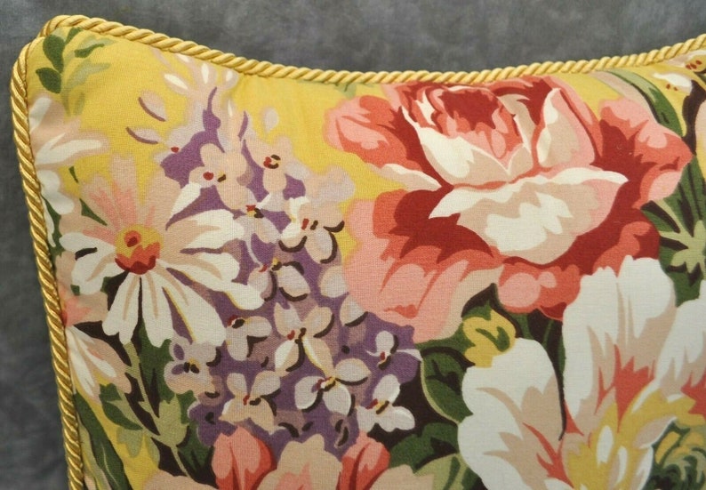 May include: A yellow pillow with a floral pattern featuring pink, red, white, and purple flowers. The pillow has a gold trim around the edges.