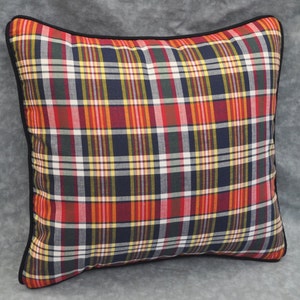 May include: A square pillow with a black trim and a plaid pattern in shades of red, yellow, blue, and green.