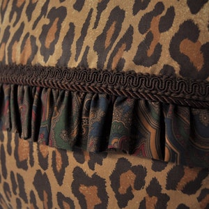 K&ouml;nnte beinhalten: Ein braunes und hellbraunes Kissen mit Leopardenmuster, braunem R&uuml;schenbesatz und darunterliegendem Stoff mit Paisley-Muster.