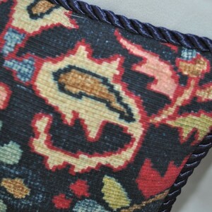 Puede incluir: Primer plano de una almohada azul oscuro con un estampado floral colorido y un ribete azul marino.