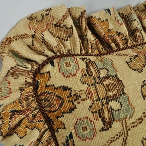 May include: A close-up of a decorative cushion with a brown, beige and blue floral pattern. The cushion has a ruffled edge and a brown trim.