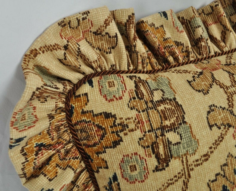 May include: A close-up of a decorative cushion with a brown, beige and blue floral pattern. The cushion has a ruffled edge and a brown trim.