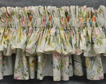 May include: A white ruffled valance with a floral print featuring pink, yellow, and blue flowers. The valance has a gathered look and is made of a soft, lightweight fabric.
