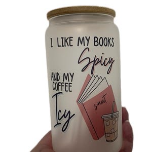 May include: White frosted glass jar with a bamboo lid. The jar has a pink and black graphic with the text "I like my books Spicy and my coffee Icy". The graphic includes a book with the word "smut" on it and a glass of iced coffee.