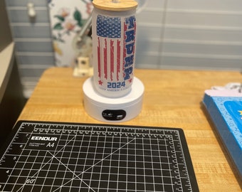 Glazen Trump 2024-beker met bamboedeksel en rietje.