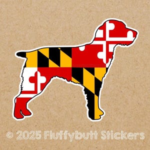 May include: A sticker in the shape of a dog, featuring the Maryland state flag design. The flag's colors of red, white, black, and yellow are prominently displayed. The sticker has a white border and is on a tan background.