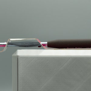 Peut inclure: Un crochet en argent avec une poign&eacute;e noire est pr&eacute;sent&eacute; sur un support blanc. Le crochet est plac&eacute; dans un support en plastique transparent.