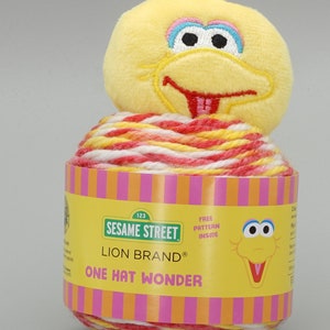 May include: A ball of red, white, and yellow yarn with a Sesame Street Big Bird plush toy on top. The yarn label reads "123 Sesame Street Lion Brand One Hat Wonder Free Pattern Inside".