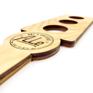 May include: Wooden beer tap handle with three holes for holding glasses. The handle is engraved with the text "Art's Awesome Ale" and a circle with the text "Fine Brewed" and "Est. 2023".