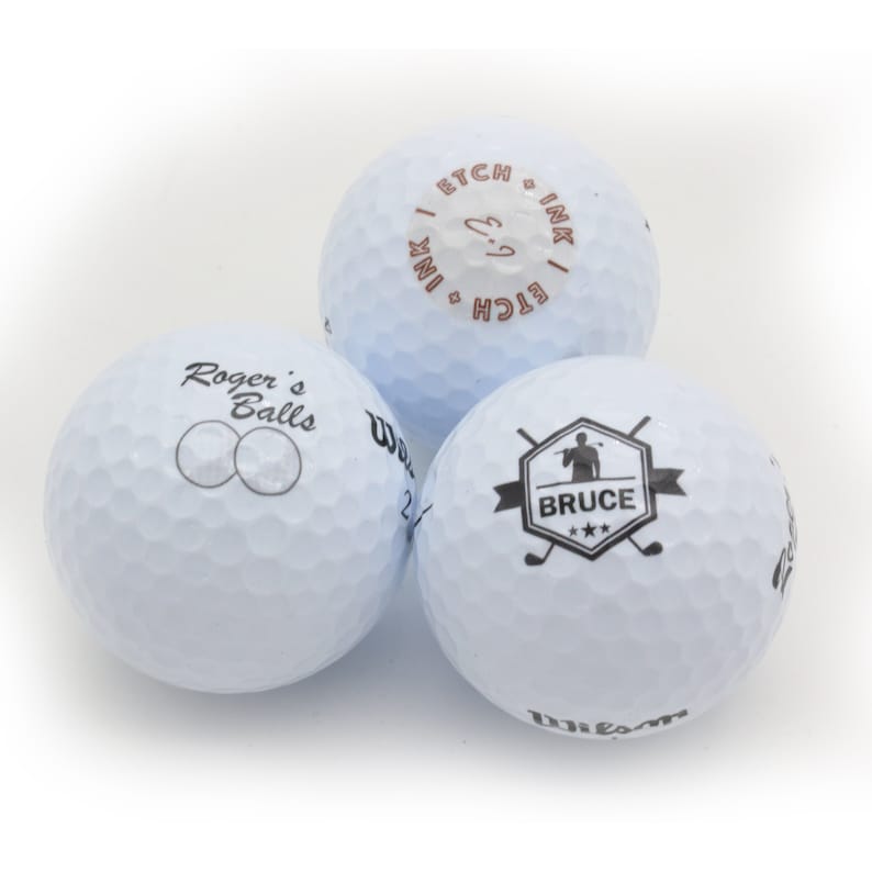 May include: Three white golf balls with different designs. One ball has the text "Roger's Balls" printed on it. Another ball has the text "Etch & Ink" printed on it. The third ball has a graphic of a golfer with the text "Bruce" printed on it.