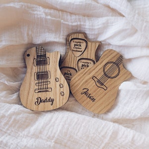 Puede incluir: Tres objetos de madera con forma de guitarra con diseños grabados. Uno dice "Daddy", otro tiene grabado "Jason", y el tercero tiene texto dentro de formas de púa de guitarra que dice "I couldn't pick a better husband" y "I'd pick you every time".