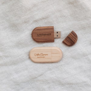 Puede incluir: Dos unidades flash USB de madera, una con el texto "Untamed Creations" y la otra con el texto "Outback Impressions Photography".