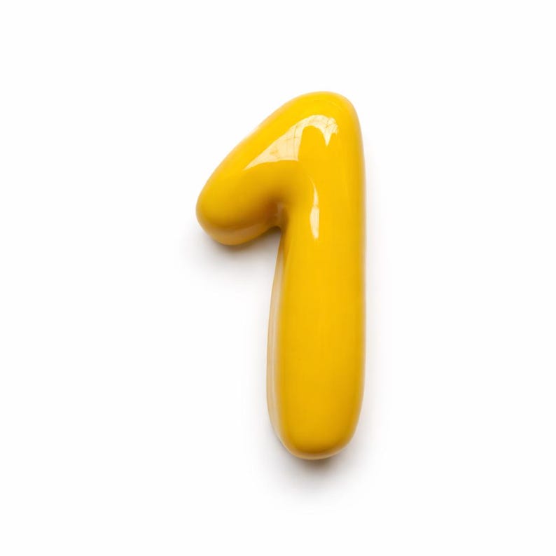 May include: A three-dimensional number one digit with a smooth, glossy finish and a vibrant yellow colour. The numeral features rounded edges and a curved top section, creating a soft, inflated appearance against a plain white background.