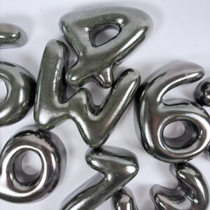 Może przedstawiać: Kolekcja tr&oacute;jwymiarowych, metalicznych srebrnych cyfr o gładkim, zaokrąglonym i wypukłym wyglądzie. Cyfry są ułożone w grupę i posiadają błyszczące wykończenie, kt&oacute;re odbija światło na ich zakrzywionych powierzchniach.