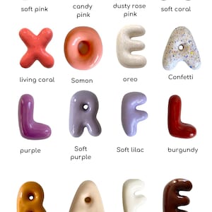 May include: A selection of glossy letter sculptures in a range of colours, such as soft pink, candy pink, dusty rose, and soft coral. Each letter has a unique design and is labelled with its colour name. The letters are arranged in a grid.