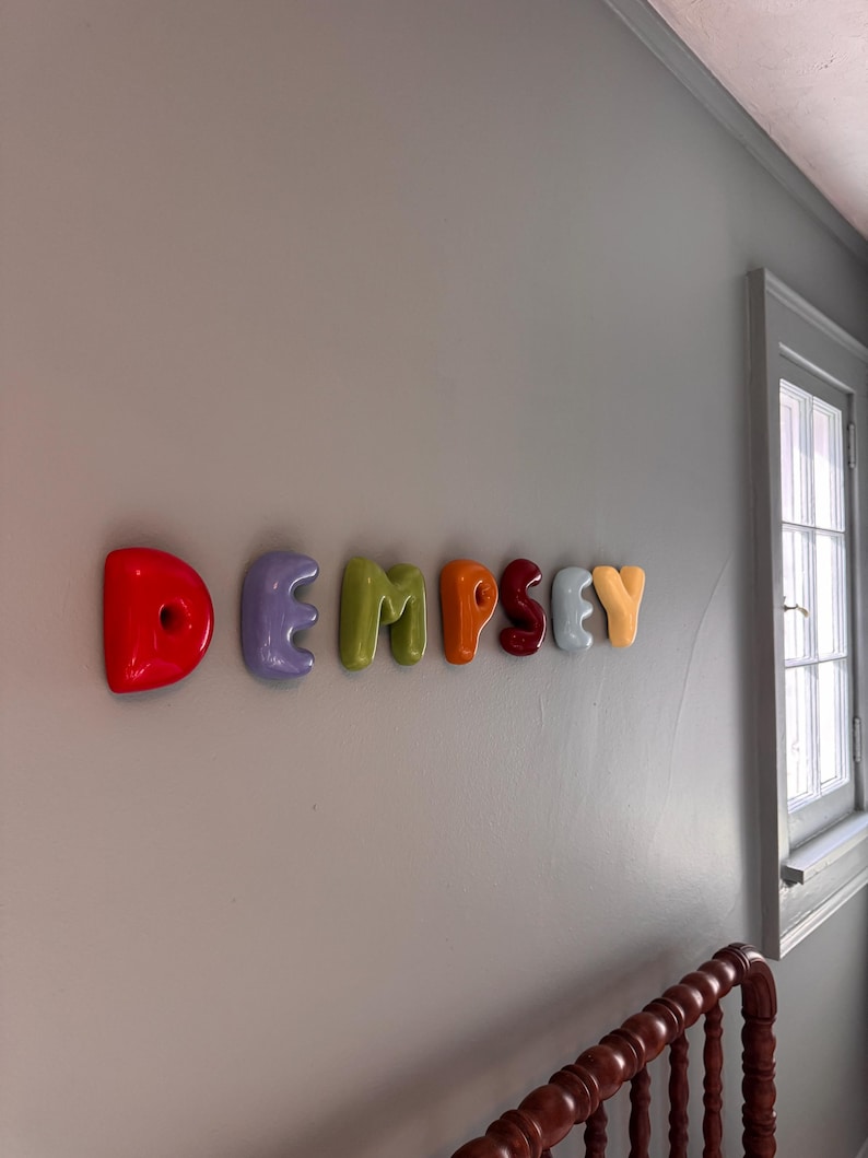 May include: A set of wall-mounted letters spelling the name DEMPSEY. Each letter features a smooth, rounded, balloon-like shape in a distinct color, including red, lavender, lime green, orange, dark red, light blue, and yellow.