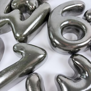 Może przedstawiać: Zbi&oacute;r tr&oacute;jwymiarowych, metalicznych srebrnych cyfr o gładkim, błyszczącym wykończeniu. Widoczne cyfry to duża sz&oacute;stka, czw&oacute;rka i jedynka, wszystkie z zaokrąglonymi krawędziami i odblaskową powierzchnią.