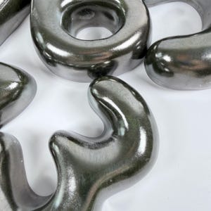 Może przedstawiać: Kolekcja gładkich, ciemnych metalicznych obiekt&oacute;w o organicznych, zaokrąglonych kształtach. Elementy mają odblaskowe, polerowane wykończenie oraz nieregularne, płynne kontury, kt&oacute;re tworzą serię połączonych ze sobą rzeźbiarskich form.